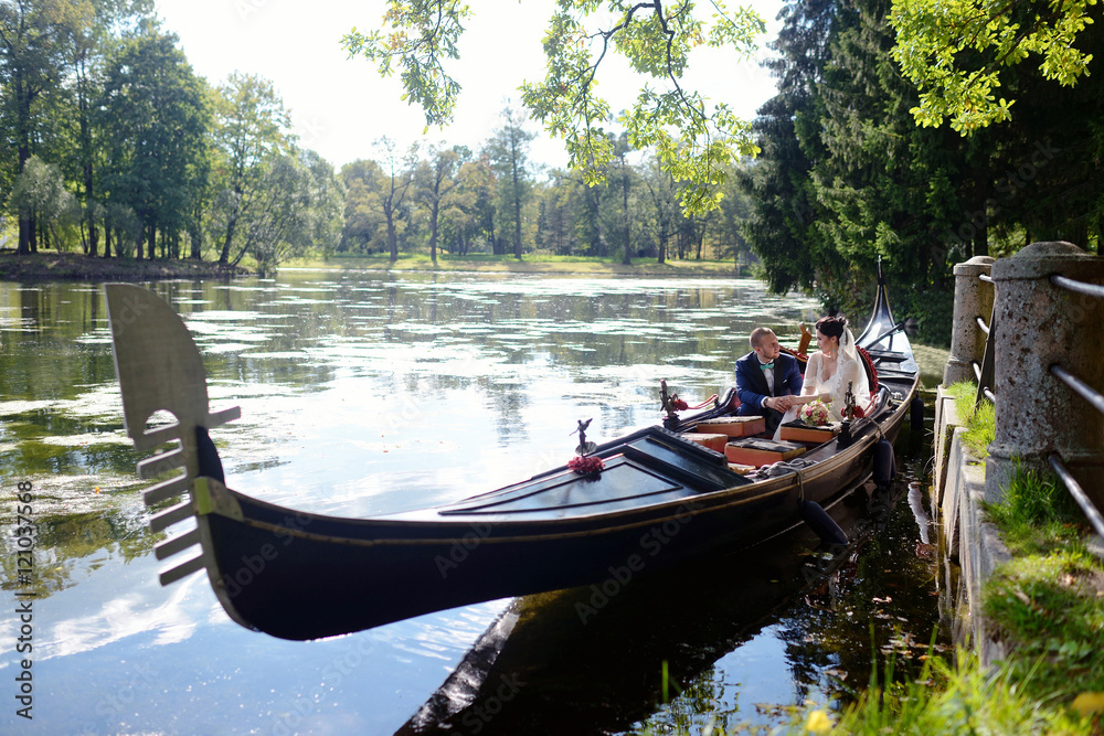 Wedding couple is hugging on a floating gondola. Beauty bride with groom. Beautiful model girl in white dress. Man in suit. Female and male portrait. Woman with lace veil. Cute lady and guy outdoors Wedding couple is hugging on a floating gondola. Beauty bride with groom. Beautiful model girl in white dress. Man in suit. Female and male portrait. Woman with lace veil. Cute lady and guy outdoors