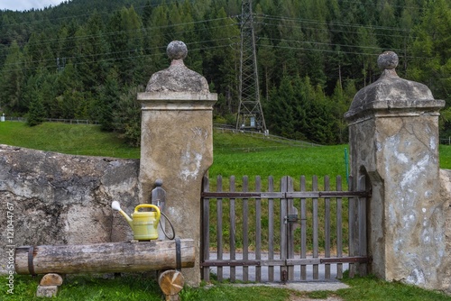 Holzbrunnen mit Gießkanne an Friedhofsmauer photo
