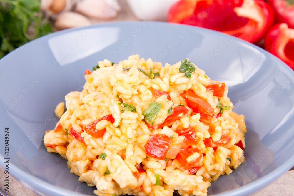 Risotto with chicken, tomatoes, bell pepper, onion, parsley and garlic on a blue plate on a wooden background Risotto with chicken, tomatoes, bell pepper, onion, parsley and garlic on a blue plate on a wooden background