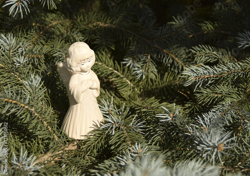 Рождественская игрушка в виде ангела. Игрушка расположена на елке. Ангел в белой одежде