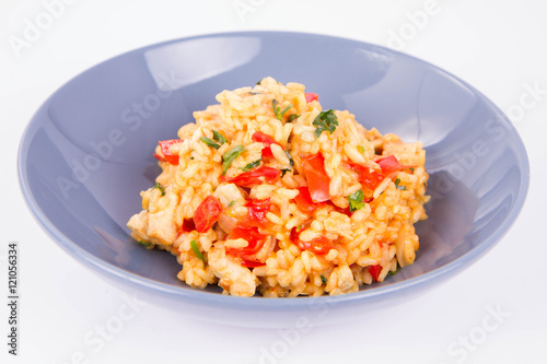 Risotto with chicken, tomatoes, bell pepper, onion, parsley and garlic on a blue plate on a wooden background