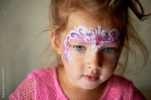 Pretty exciting blue-eyed girl of 2 years with a pink face painting