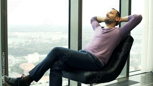Young man relaxing and admire view from window while sitting on chair at home
