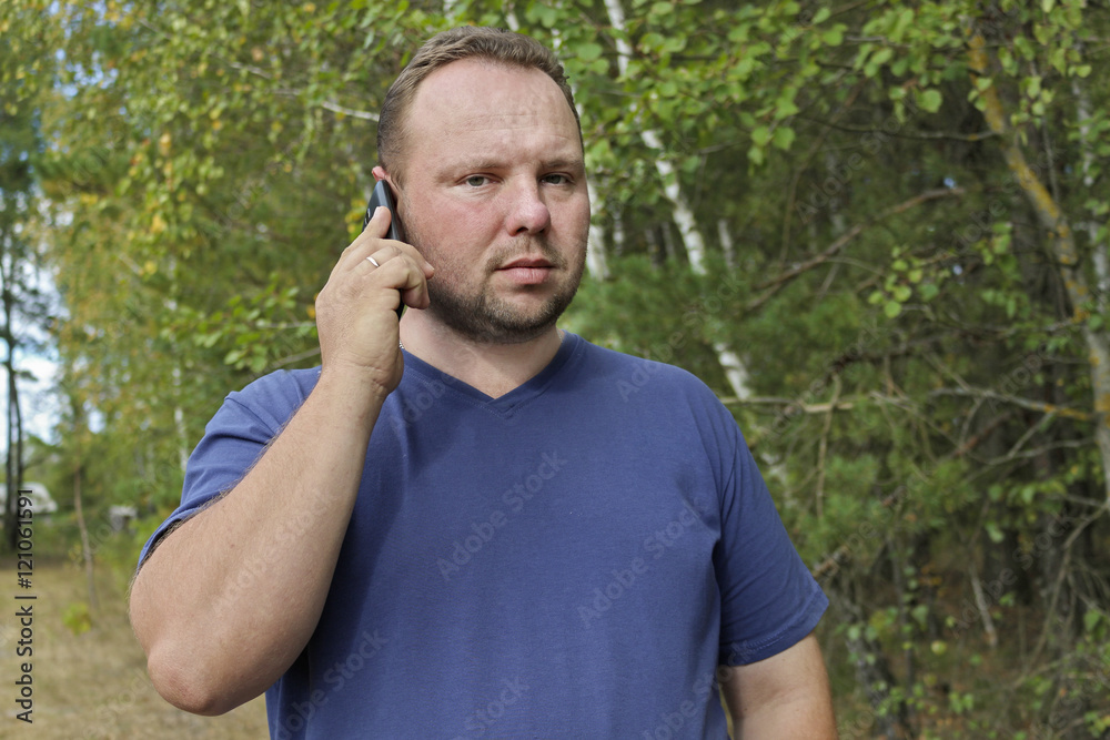 Young man talking on mobile phone in nature, green background. Communication without borders and outside the city.The unshaven man. Young man talking on mobile phone in nature, green background. Communication without borders and outside the city.The unshaven man.