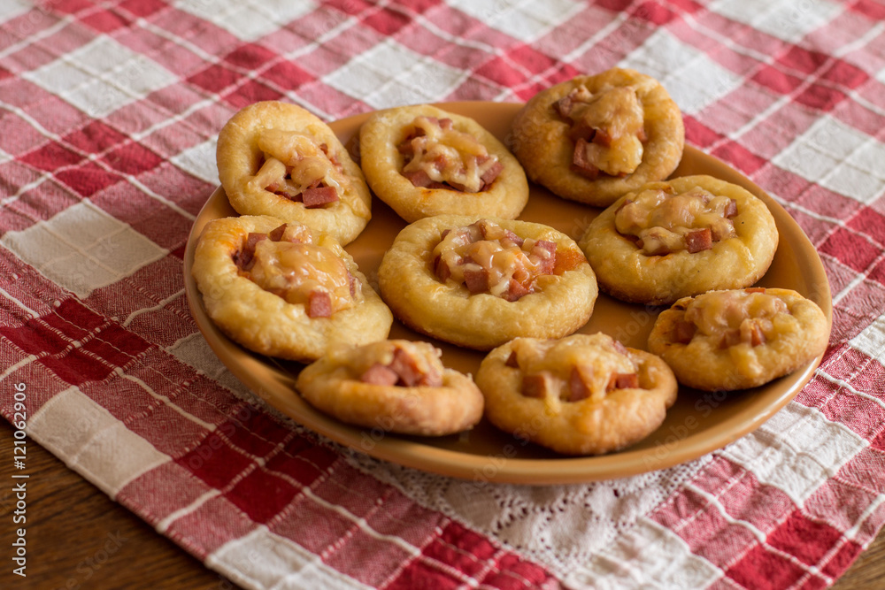 Mini pizzas with sausage and cheese in orange plate on checkered tablecloth. Mini pizzas with sausage and cheese in orange plate on checkered tablecloth.
