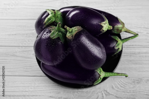 Plate with fresh aubergines on wooden background, top view