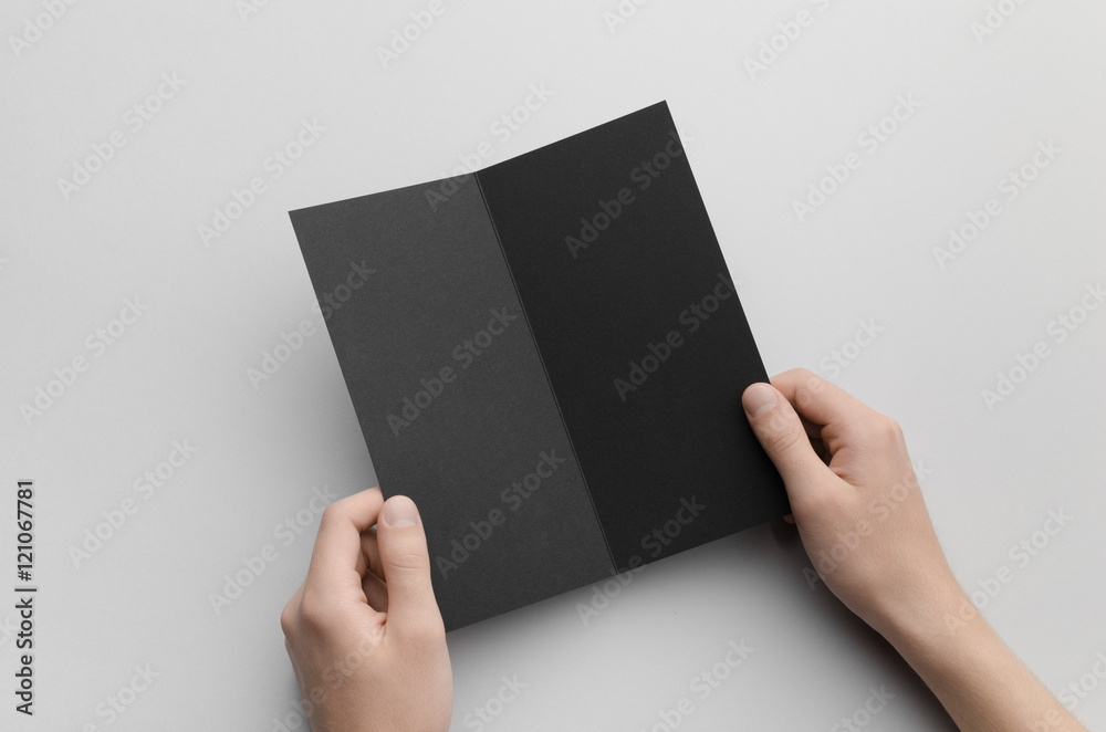 Black DL Bi-Fold Brochure Mock-Up - Male hands holding a black bi-fold on a gray background. Black DL Bi-Fold Brochure Mock-Up - Male hands holding a black bi-fold on a gray background.