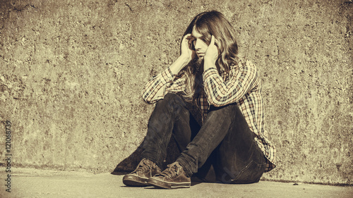 Man long haired sitting alone sad on grunge wall