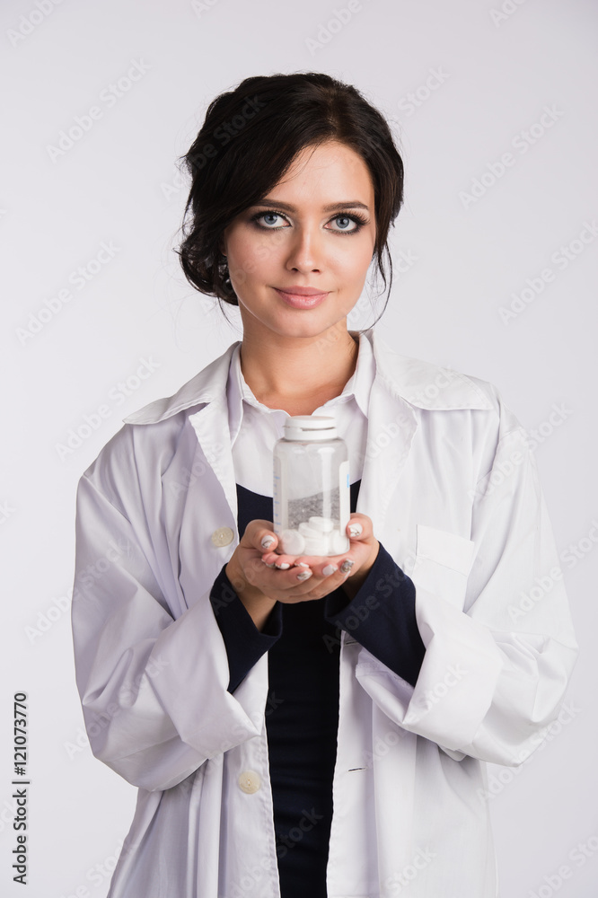 Beautiful young brunette female nurse or physician with glasses in blue dress and white lab coat holding a bottle of pills Beautiful young brunette female nurse or physician with glasses in blue dress and white lab coat holding a bottle of pills