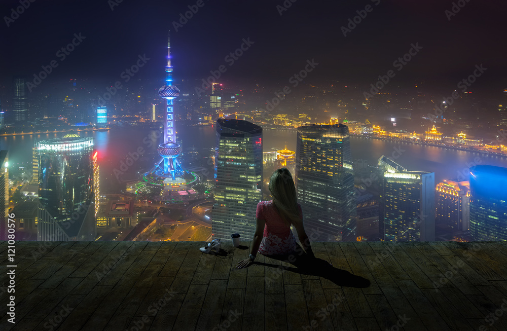 Fototapeta premium Kobieta siedzi na dachu z filiżanką kawy i enjoing widok na noc Szanghaj.