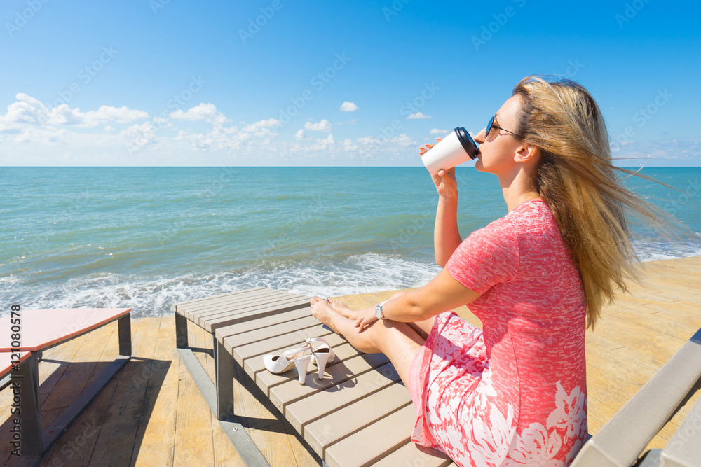 Young beautiful woman sitting on the beach chair with shoes and drink coffee. Young beautiful woman sitting on the beach chair with shoes and drink coffee.