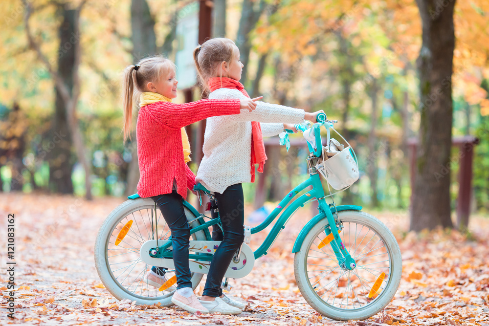 Obraz premium Two adorable girls in park at warm sunny autumn day. Kids on bicycle together