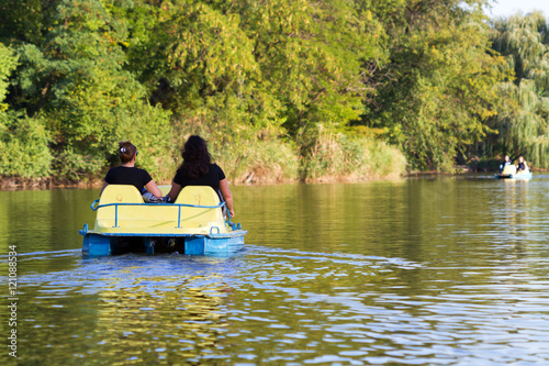 Women ride on yellow pedal catamaran on the river in autumn park