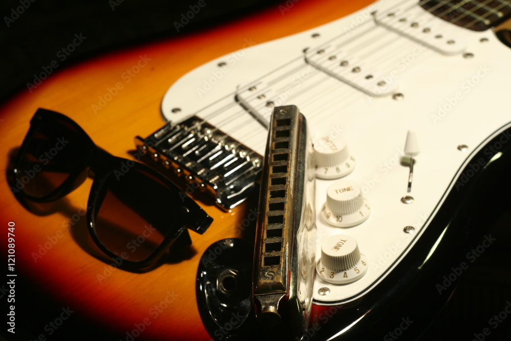 Vintage electric guitar, harmonica, sunglasses on black background