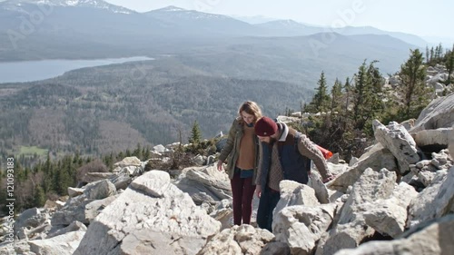 Slow motion shot young man with beard and his blond girlfriend walking on unsteady rocks and trying to find trail high up in mountains 