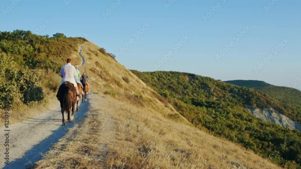Group of people ride horses by gorgeous mountainside trail. Family on horseback riding trip on mountain trail Group of people ride horses by gorgeous mountainside trail. Family on horseback riding trip on mountain trail