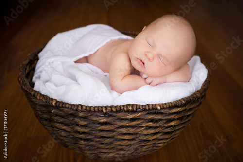 Portrait of adorable newborn baby boy sleeping in a wicker basket.