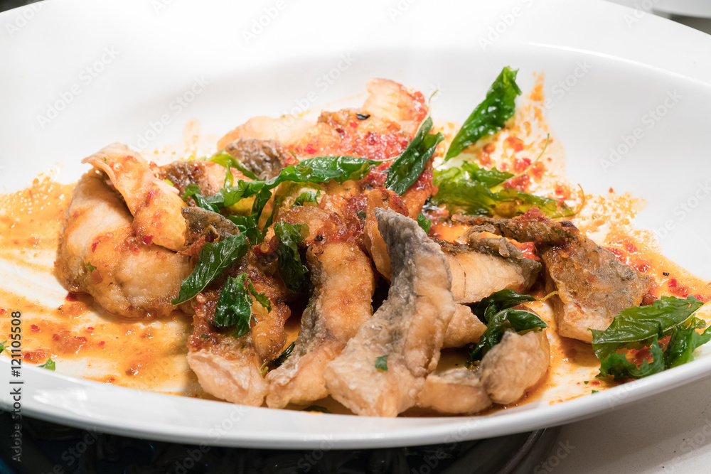Fried fish in spicy curry sauce on white dish
