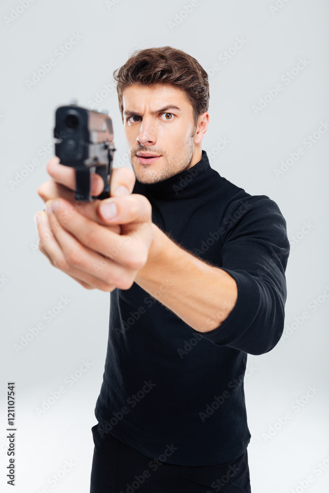 Concentrated young man standing and pointing with gun on you Concentrated young man standing and pointing with gun on you