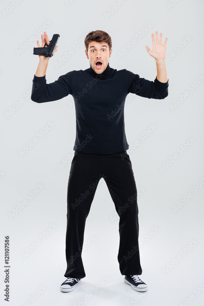 Scared young man holding gun and standing with hands up Photos