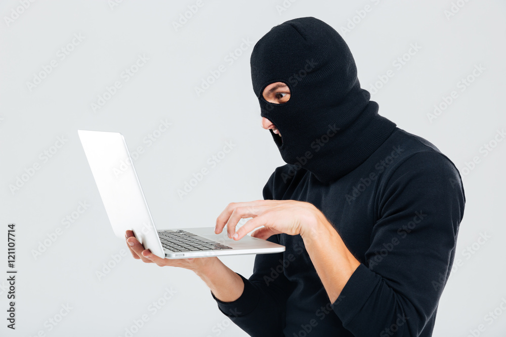 Portrait of man in balaclava standing and using laptop Portrait of man in balaclava standing and using laptop