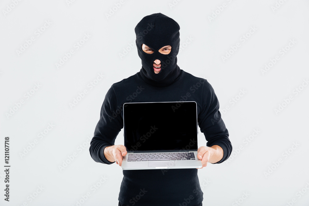 Criminal man in balaclava holding blank screen laptop Criminal man in balaclava holding blank screen laptop