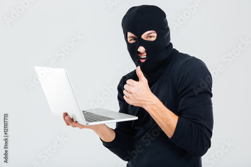 Canvas Print Man in balaclava using laptop and showing thumbs up