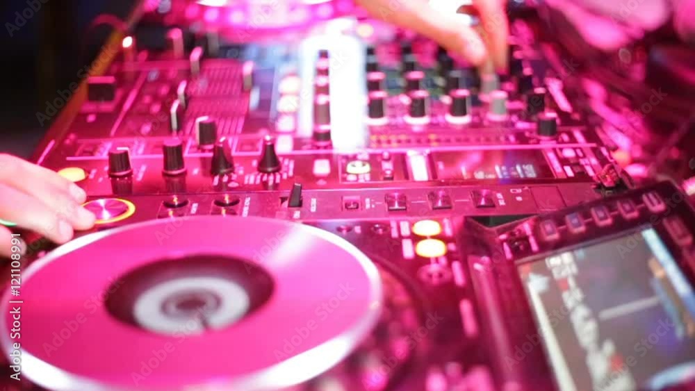 Mani di un disk Jockey che sta premendo pulsanti e ruotando pomelli sulla sua consolle durante una festa in discoteca notturna. Illuminazione con luci fucsia artificiali.