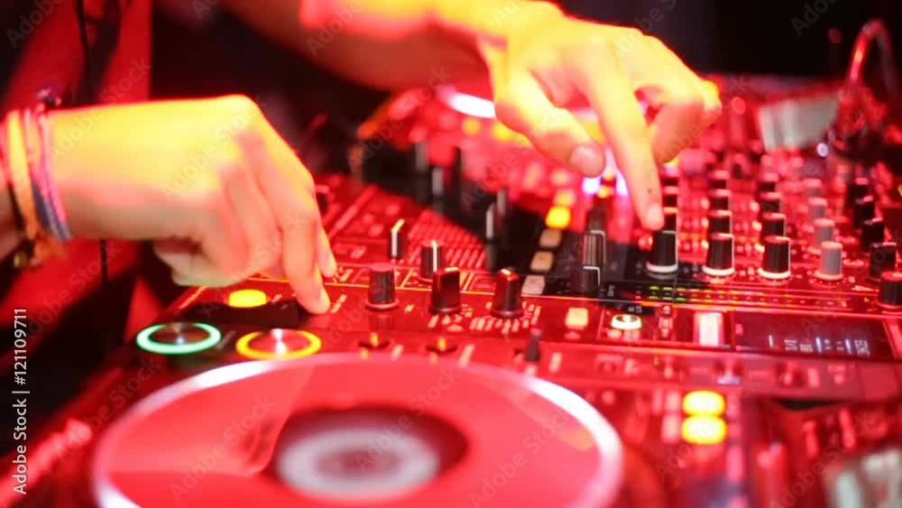 Mani di un disk Jockey che sta premendo pulsanti e ruotando pomelli sulla sua consolle durante una festa in discoteca notturna. Illuminazione con luci rossi artificiali.