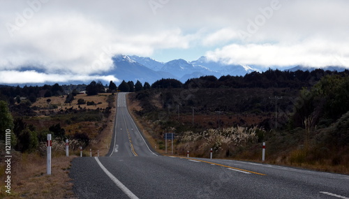 Country road at the alps in New Zealand South Island. Mountains of Fiordland National Park in the background.