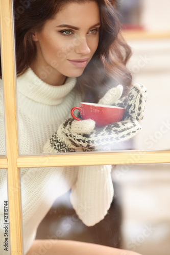 woman drinking coffee and looking out of the window on winter da