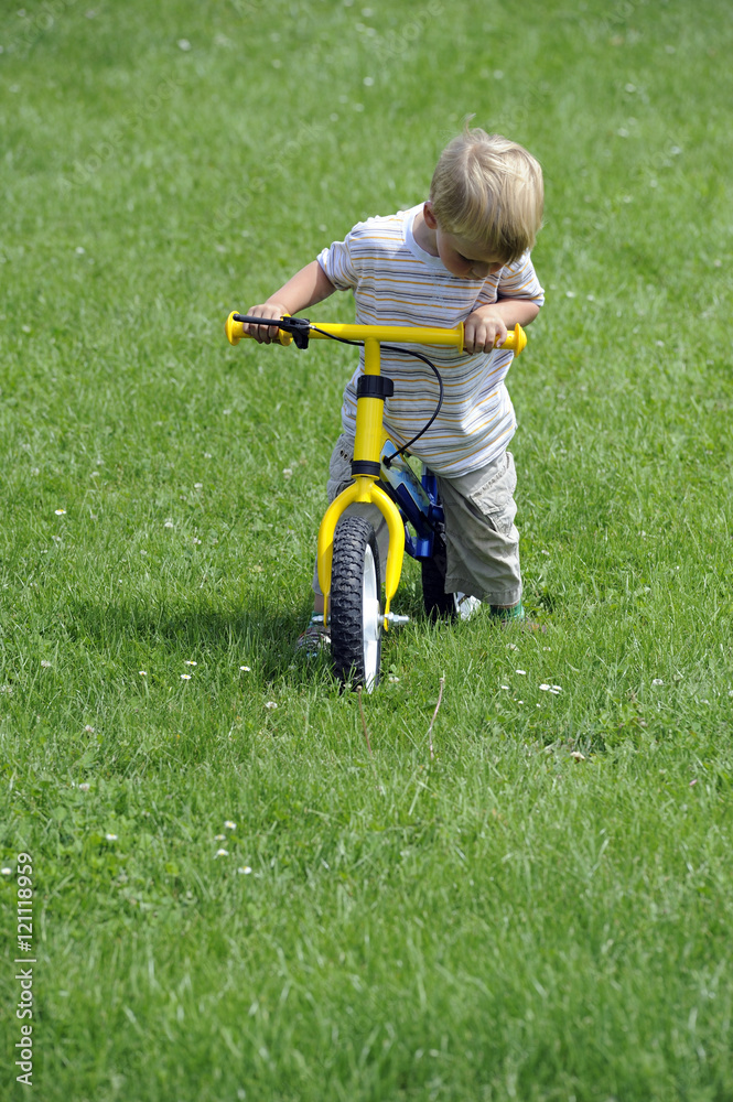 Child boy riding on his first bike with a helmet. Bike without pedals. Child learning to ride and balance on his two wheeler bike with no pedals. Child boy riding on his first bike with a helmet. Bike without pedals. Child learning to ride and balance on his two wheeler bike with no pedals.