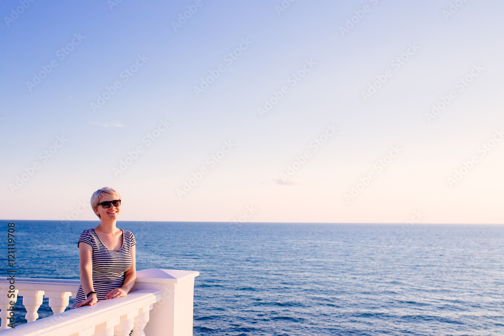 cute blondy woman on balcony looking at the ocean. travel concept
