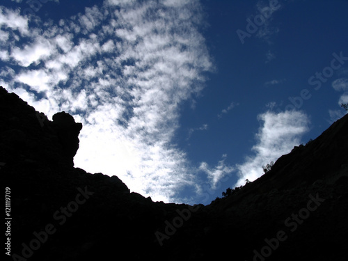 Blue sky with white clouds and black mountain silhouette