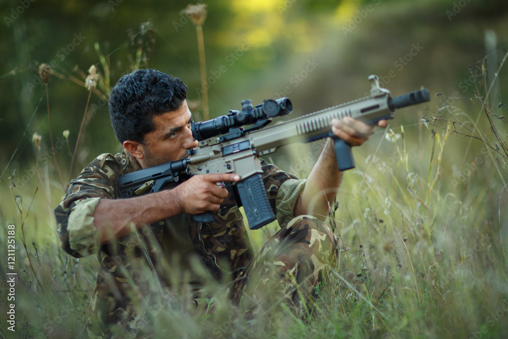 Fototapeta premium Man of Arab nationality in camouflage with a gun aiming at a tar