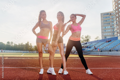 Group of fit young sportswomen standing on athletics stadium and posing.