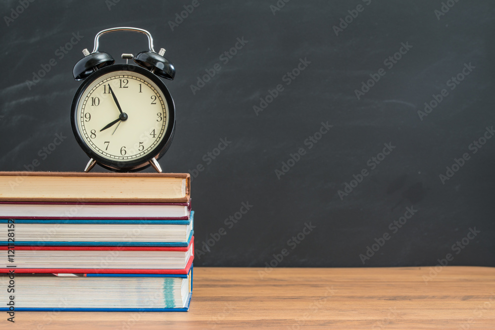 alarm clock and book on student desk in front of blackboard alarm clock and book on student desk in front of blackboard