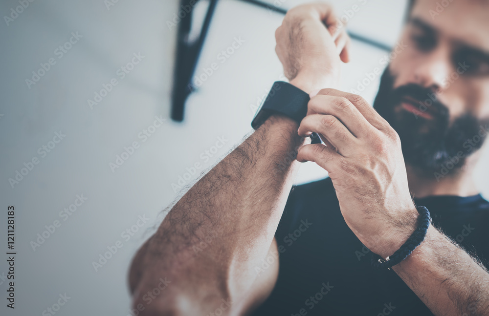 Close-up Shot Young Bearded Sportive Man After Workout Session Checks Fitness Results Smart Watch.Adult Guy Athlete Wearing Sport Tracker.Training hard gym.Horizontal bar background.Blurred.