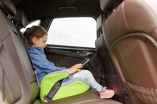 happy little girl with tablet pc driving in car