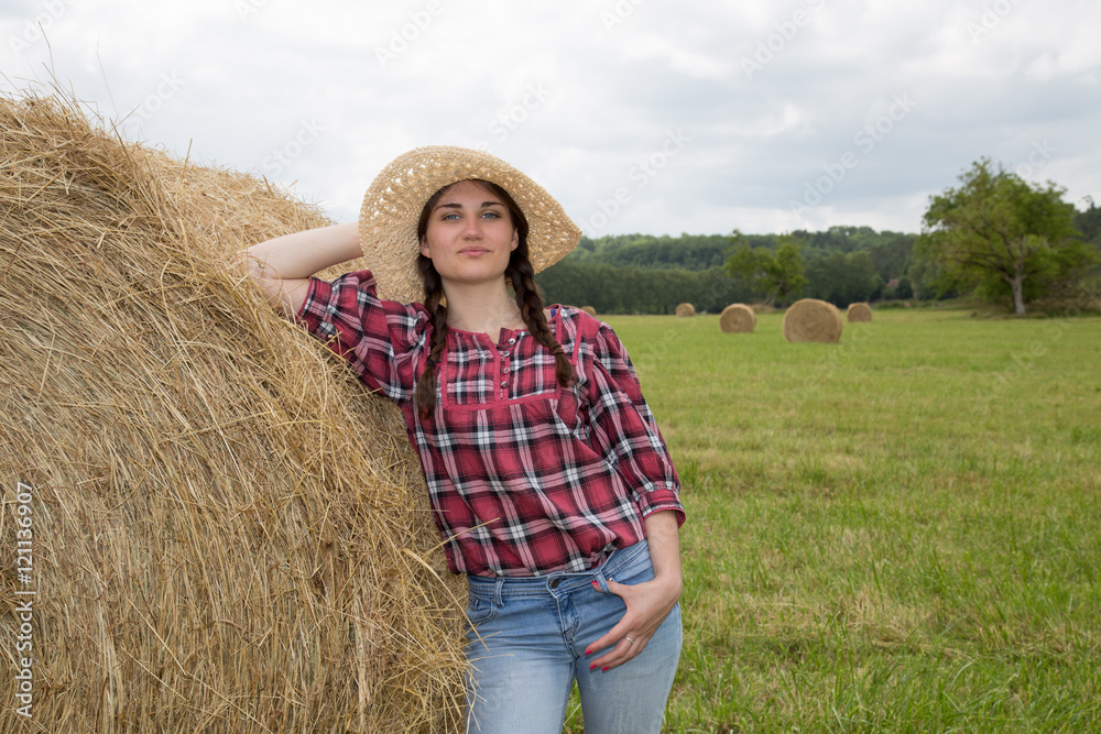 Portrait of young woman standing next to a stack of hay in sunlight Portrait of young woman standing next to a stack of hay in sunlight