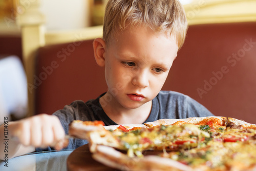 Adorable little boy eating pizza at a restaurant