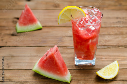 Slices of watermelon and ice cubes in a glass on a wooden table.