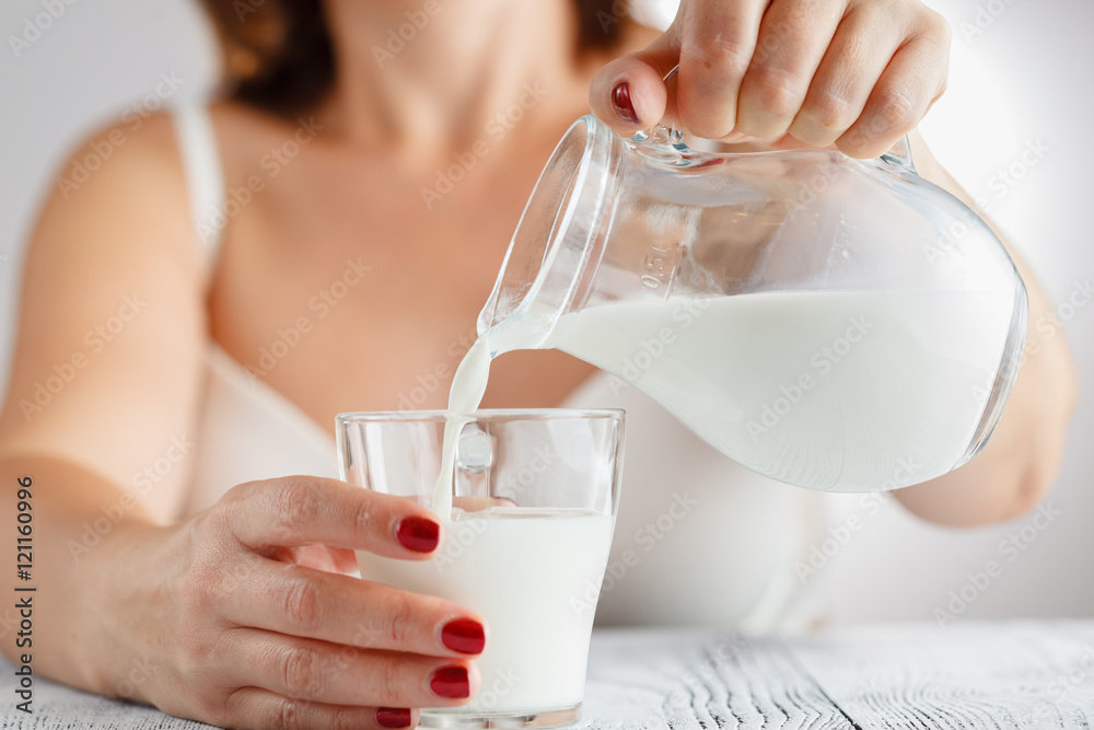 Womans hand pouring milk from a jug in a glass Womans hand pouring milk from a jug in a glass