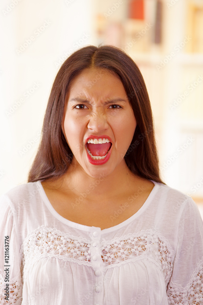 Beautiful young brunette woman wearing white blouse top, interacting screaming towards camera, bright household background Beautiful young brunette woman wearing white blouse top, interacting screaming towards camera, bright household background