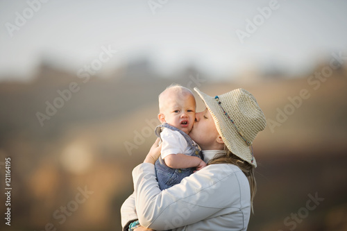 Portrait of a young adult woman wearing a hat kissing her baby boy. photo