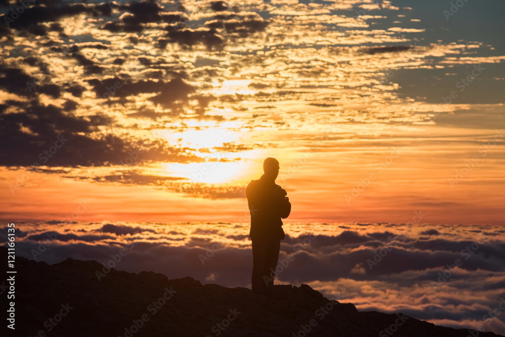 Young man on sunset above the clouds in the mountains
