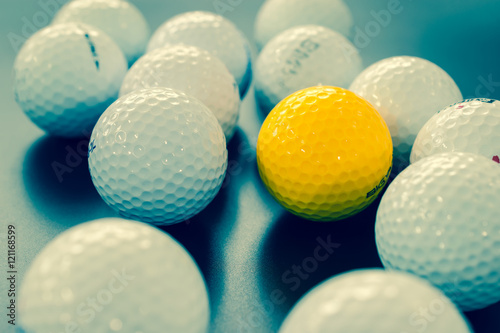 white and one yellow golf balls on black floor. individuality an
