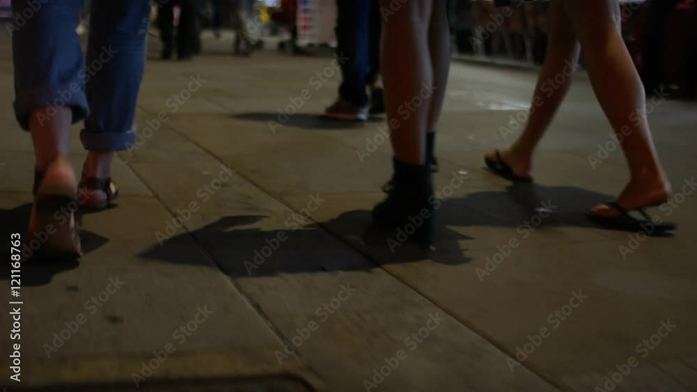 Legs of three females walking along a sidewalk in the city at night