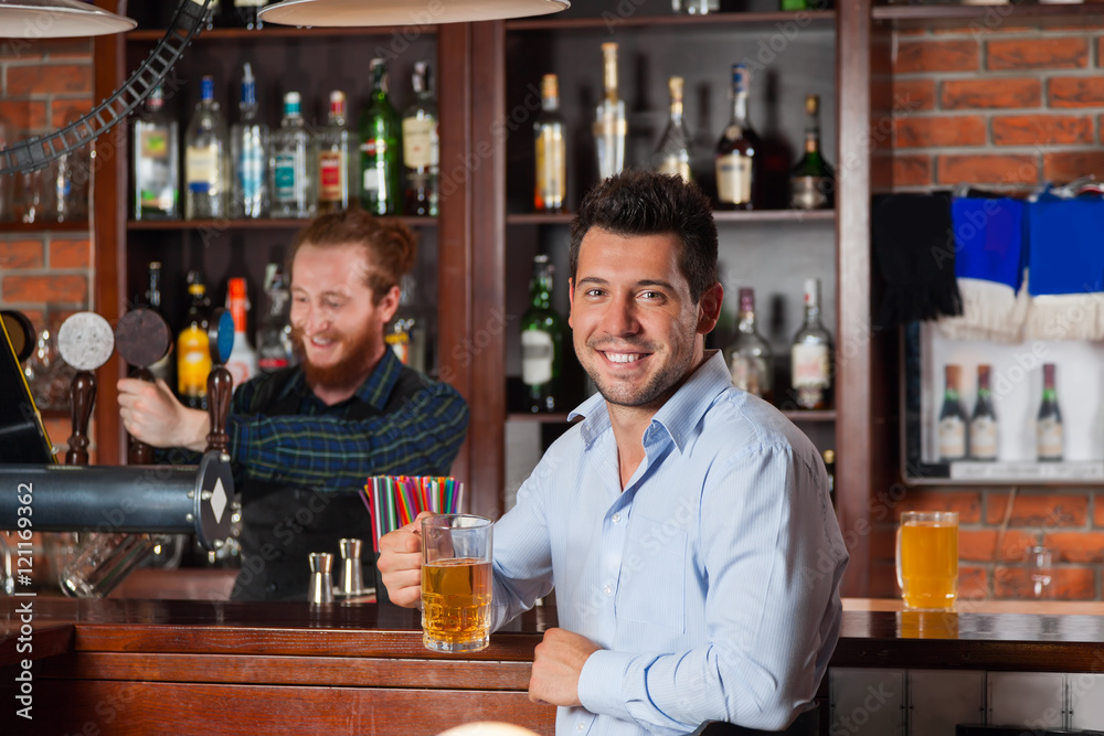 Young Man In Bar Hold Glasses Sit At Counter, Drinking Beer Young Man In Bar Hold Glasses Sit At Counter, Drinking Beer
