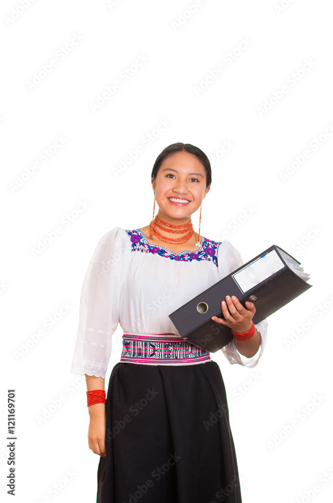 Beautiful young woman standing wearing traditional andean blouse and red necklace, holding black ring binder while smiling happily, white studio background Beautiful young woman standing wearing traditional andean blouse and red necklace, holding black ring binder while smiling happily, white studio background